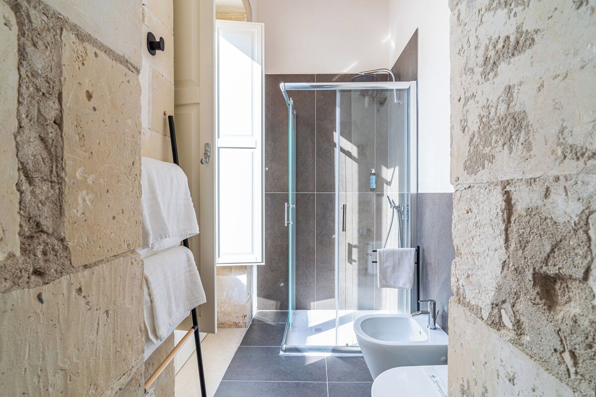 A bathroom with a glass shower enclosure, a bathtub, and stone walls.