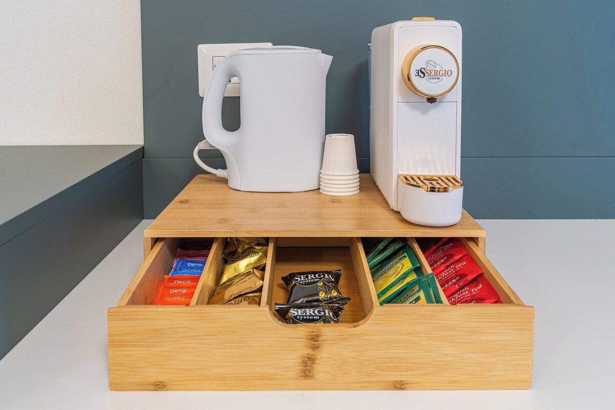 Een houten lade met vakken, gevuld met verschillende spullen zoals een koffiezetapparaat, een mok en zakjes thee.