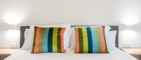 A bed with white bedding and two pillows with multicolored stripes.
