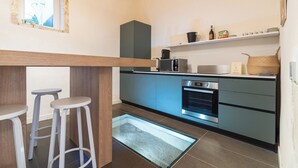 Eine moderne Küche mit Einbauofen, Mikrowelle und Kaffeemaschine. Zwei Barhocker und ein Holztisch sind ebenfalls vorhanden.