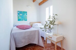 Un dormitorio con dos camas, una mesita de noche con lámpara, un cuadro en la pared y una ventana.