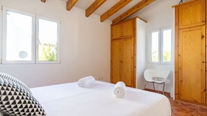 Een slaapkamer met een bed, twee ramen, een houten garderobe en een stoel.