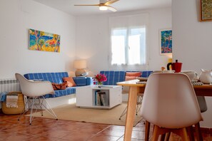 Una sala de estar moderna con un sofá azul, sillones blancos, una mesa de centro y una mesa de comedor.
