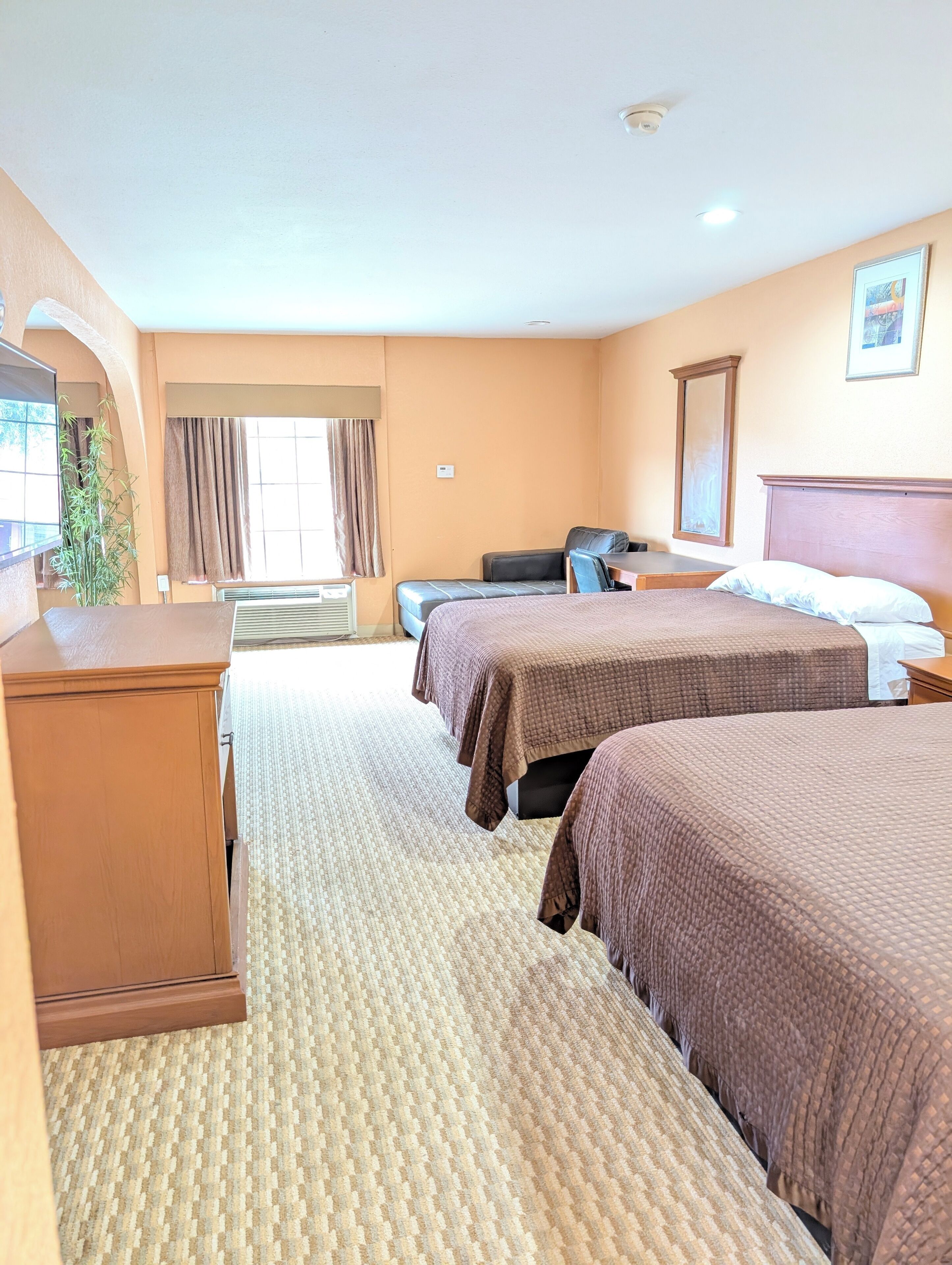 A hotel room with two beds, a desk, a chair, a dresser, and a window with curtains.