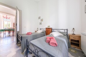 A room with two beds, a wooden nightstand, a radiator, and a door leading to a dining area. - Villa 'La Casa Bianca' with Private Terrace, Wi-Fi and Air Conditioning (Lipari)
