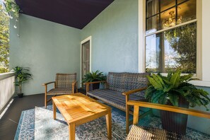 A covered outdoor seating area with a wooden table and two wicker chairs, a woven sofa, and potted plants. - Ever After: Luxury, Romantic Unit + Walk Downtown (Staunton)