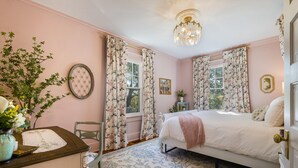A bedroom with a bed, floral curtains, a chandelier, and a vase with flowers.