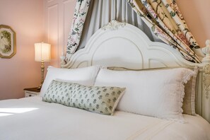 Una cama bien hecha con almohadas de estampado floral, un cabecero blanco y una mesita de noche con una lámpara.