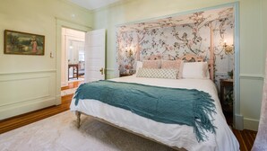 A bedroom with a large bed, floral wallpaper, and a chandelier.