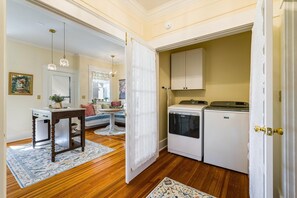 A compact kitchen with white appliances, a wooden table, and a decorative rug.