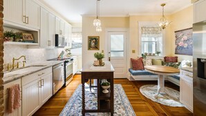 A kitchen with white cabinetry, a central island with a sink, a chandelier, and a dining area with a bench.