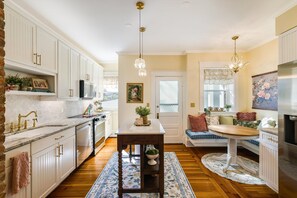 A kitchen with white cabinetry, a central island with a sink, a chandelier, and a dining area with a bench.