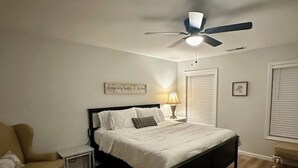 Ein Schlafzimmer mit Bett, Sessel, Nachttisch, Deckenventilator und einer Wand mit einem Schild.