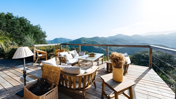 Una terraza de madera con mobiliario de mimbre, una mesa y una lámpara.