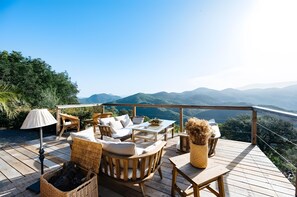 A wooden deck with wicker furniture, a table, and a lamp. - Casa Tres Sierras – Renovated Andalusian Country House with Mountain Views (Coripe)