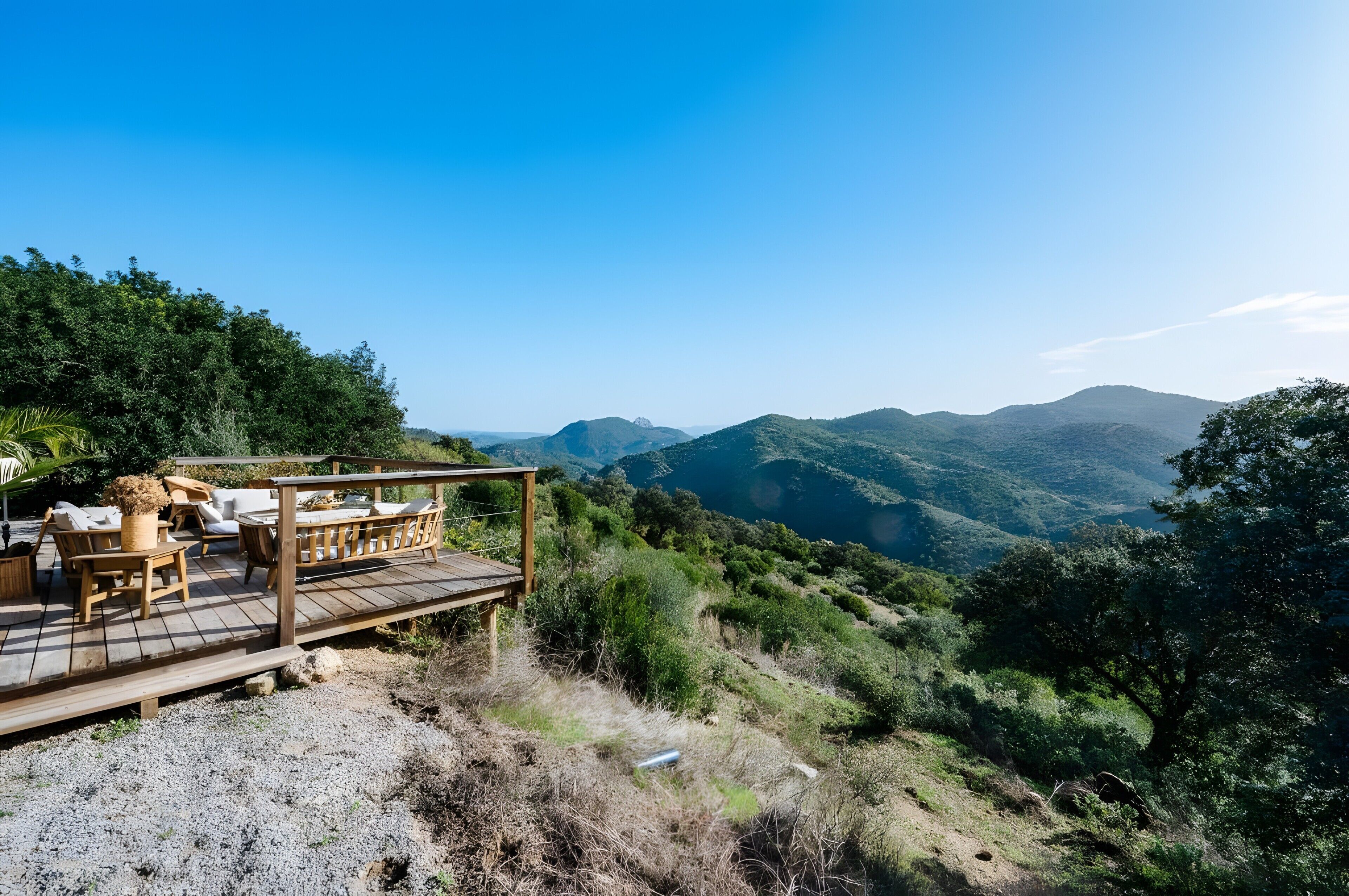 Una terraza de madera con mobiliario exterior con vistas a un paisaje montañoso.