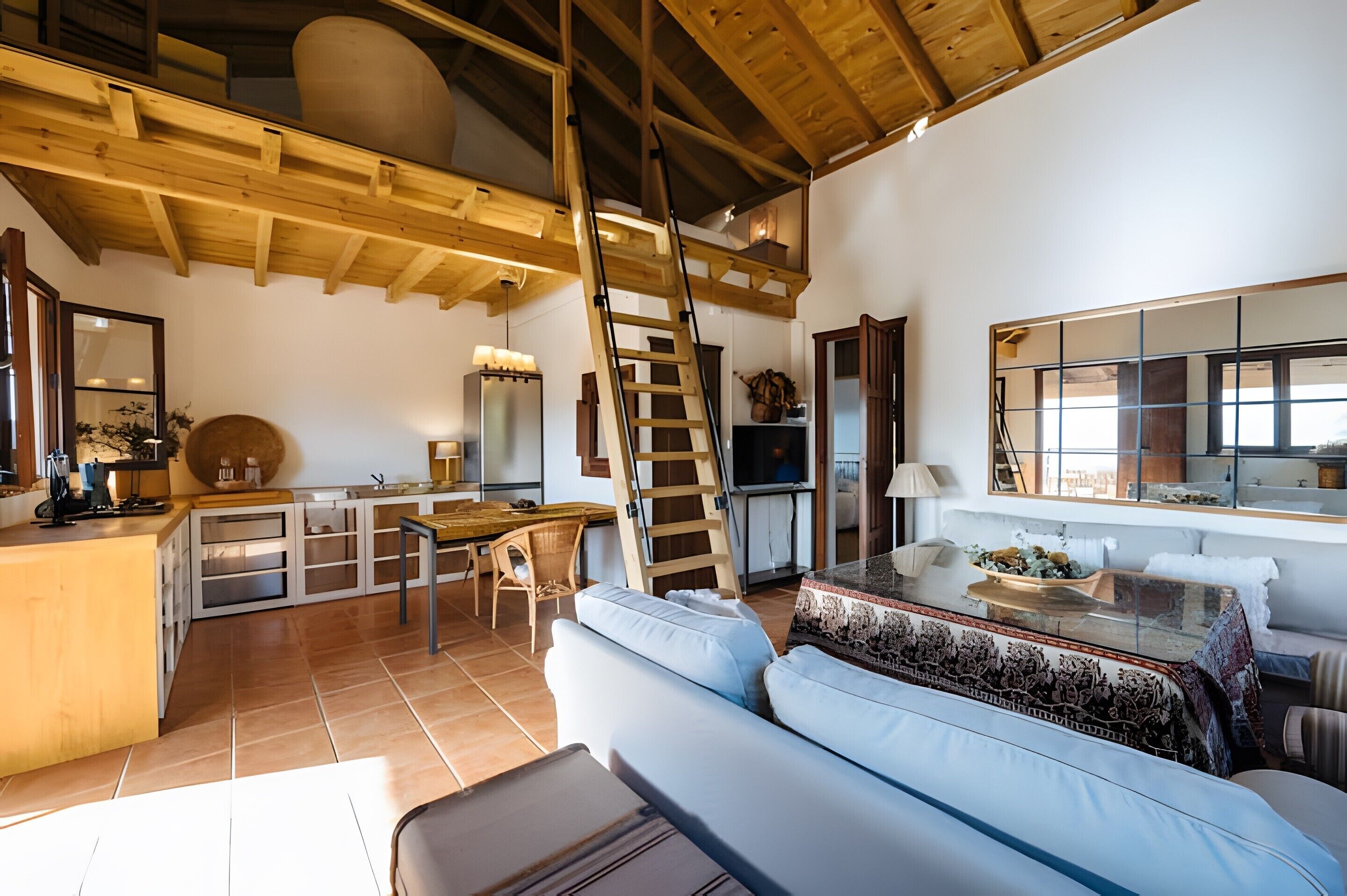 Un ampio soggiorno con soffitto in legno, una cucina con isola centrale e un'ampia finestra che offre luce naturale.
