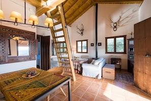 A rustic interior with a wooden ceiling, a dining table with a decorative table runner, a ladder, a sofa, and a cabinet.