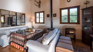 Una sala de estar acogedora con un sofá, una mesa de centro de vidrio, una chimenea, un espejo y una ventana con vistas a árboles.