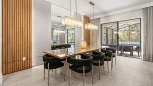 Un espace de salle à manger moderne, avec une longue table en bois, des chaises à revêtement noir et des lustres en cristal suspendus au plafond.
