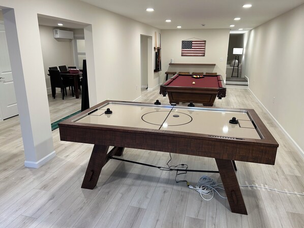 A pool table with a red felt top, a billiards table in the background, and a flag on the wall.