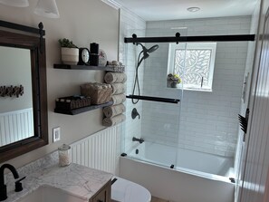 A modern bathroom with a glass-enclosed shower, a marble sink, and a window with a view.