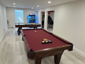 A pool table with balls, a billiards cue, and a pool table in a room with a ceiling-mounted projector.