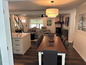 Une cuisine moderne avec un ßlot central en bois, un coin repas avec une grande table et des chaises, une cheminée et un escalier menant à un autre niveau.