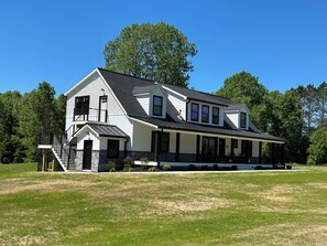 A two-story house with a porch, a stone foundation, and a large lawn.