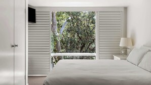 Un dormitorio con una cama grande, una mesita de noche con lámpara, un armario y una ventana con persianas.