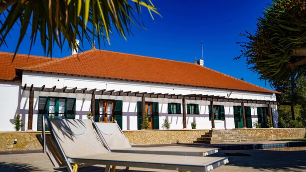 A building with a tiled roof, a stone wall, and a pool area with lounge chairs. - Quarto Rosa Duplo Deluxe (Canal Caveira)