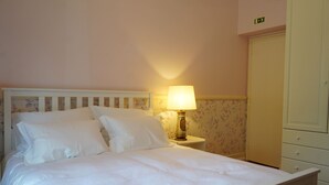 A neatly made bed with white linens in a room with floral wallpaper and a white wardrobe. - Quarto Rosa Duplo Deluxe (Canal Caveira)
