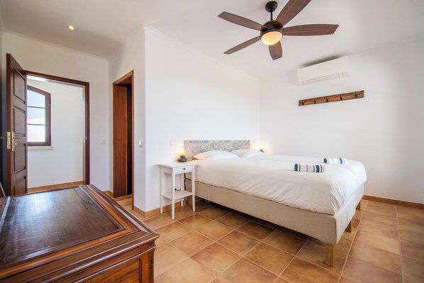 Un dormitorio con cama, mesita de noche, ventilador de techo y aire acondicionado.