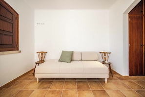 Una habitación con un sofá color crema, dos sillas de madera, un cojín verde y un armario de madera.