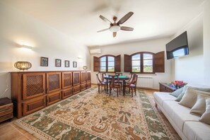 Un salon spacieux avec un grand meuble en bois, une table à manger avec des chaises, un canapé et un ventilateur de plafond.