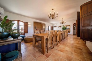 Un vaste espace dédié à la salle à manger, avec une longue table en bois et des chaises, un lustre et des plantes en pot.