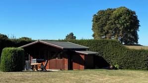 Une cabane en bois avec un toit en pente, une véranda et un petit espace patio comprenant une table et des chaises.