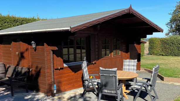 Une cabane en bois dotée d’un patio comprenant une table et des chaises, un barbecue et offrant une vue sur le paysage environnant.