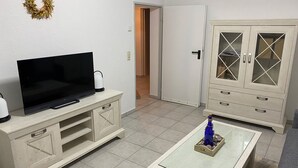 Un salon avec un téléviseur posé sur un meuble, une table basse en verre agrémentée d’objets décoratifs et une armoire aux portes en verre.