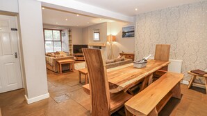 Un salón amplio con una mesa de comedor de madera, bancos y un sofá. Hay un televisor, una lámpara y una chimenea.