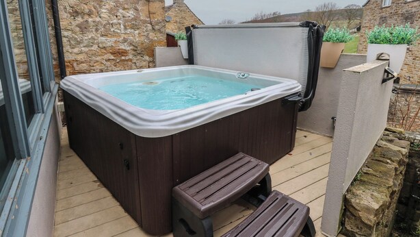 Un jacuzzi en una terraza de madera con un muro de piedra al fondo.