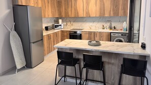 A modern kitchen with wooden cabinets, a stainless steel refrigerator, a microwave, a sink, and a built-in washing machine. There are three black chairs at the island. - Villa - Sleeps 6 - Near Local Attractions (Limassol)