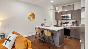 Een moderne keuken met een centraal eiland, roestvrijstalen apparatuur en een zithoek met een bank en stoelen.
