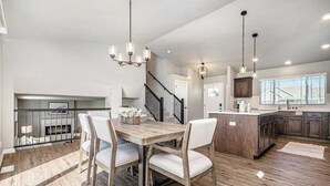 A spacious kitchen with a wooden dining table, white chairs, and pendant lighting. - Omaha Charm! Cozy Comfort home in the heartland (Chicago Precinct)