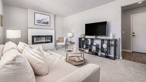 A modern living room with a beige sofa, a fireplace, a flat-screen TV, and a coffee table. - Omaha Charm! Cozy Comfort home in the heartland (Chicago Precinct)