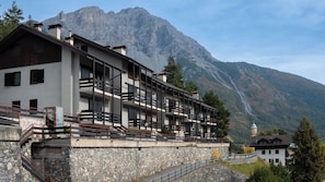 Un hôtel à plusieurs étages doté de balcons, de murs en pierre et surplombant un paysage montagneux.