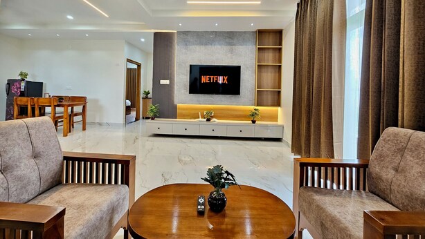 A modern living room with a flat-screen TV mounted on the wall, a wooden coffee table, and two sofas. - TrueLife Summit Suites (Tirupati)