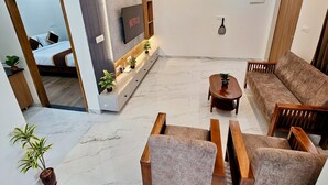A modern living room with a sofa, armchairs, a coffee table, and a TV mounted on the wall. - TrueLife Summit Suites (Tirupati)