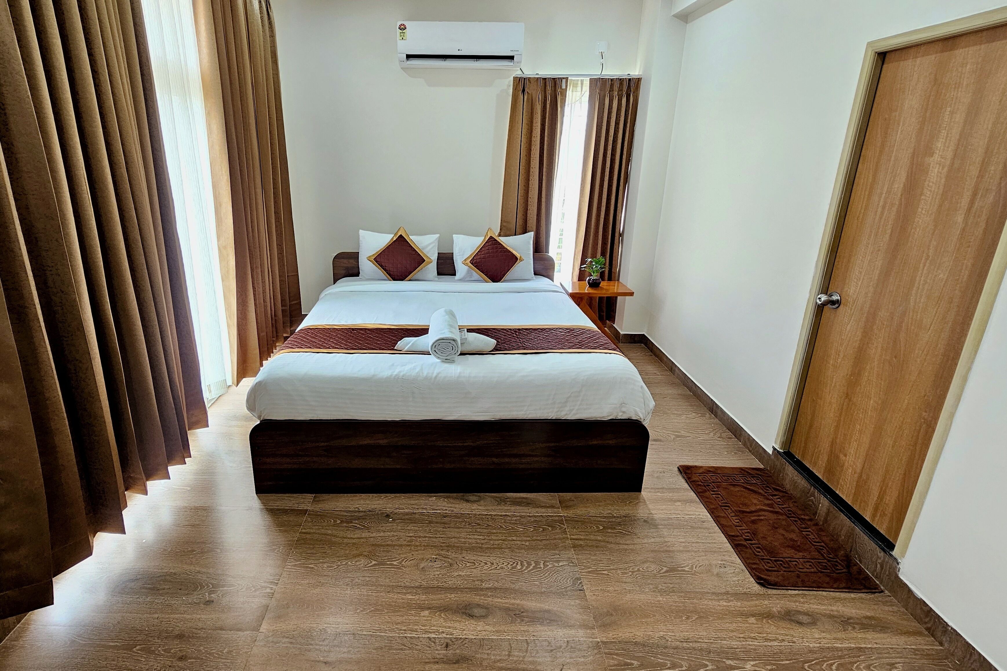 A hotel room with a large bed, brown curtains, a wooden floor, and a wooden door.