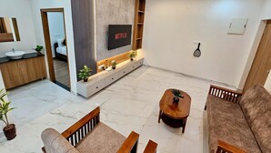 A modern living room with a sofa, coffee table, and TV mounted on the wall. - TrueLife Summit Suites (Tirupati)